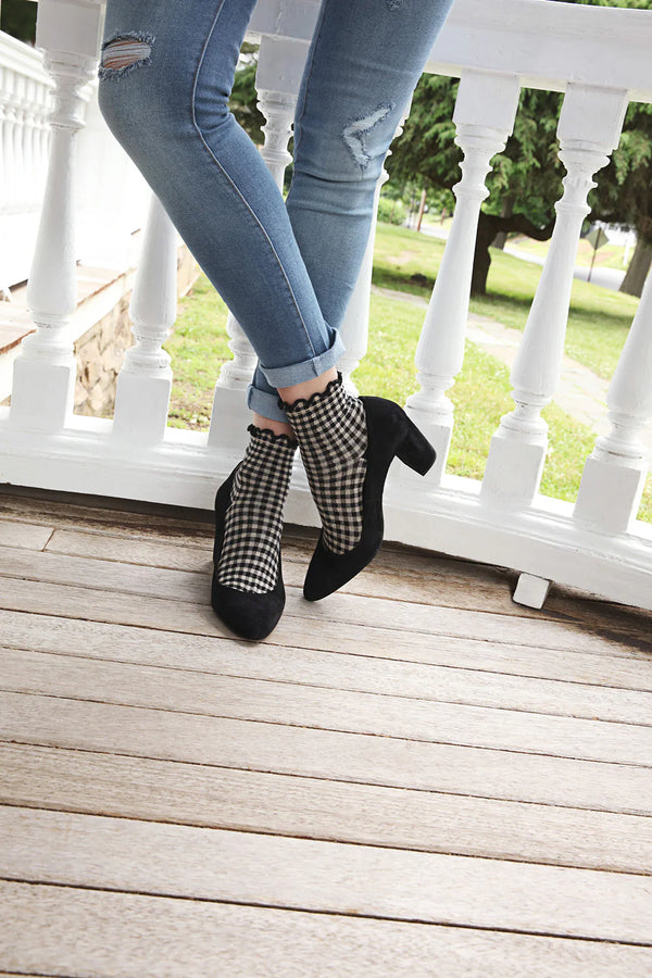 A model shown from the knees down stands cross-legged wearing jeans, black heels and black-and-beige anklets with ruffled tops.
