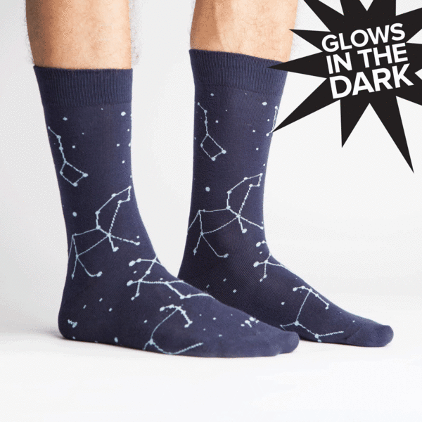 Pair of feet wears navy blue crew socks with white stars & constellations. Every few seconds the stars changed to a glow in the dark green.