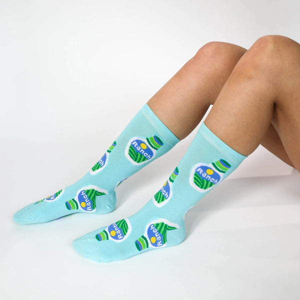 A model wearing blue novelty socks with bottles of Ranch salad dressing featured on them.