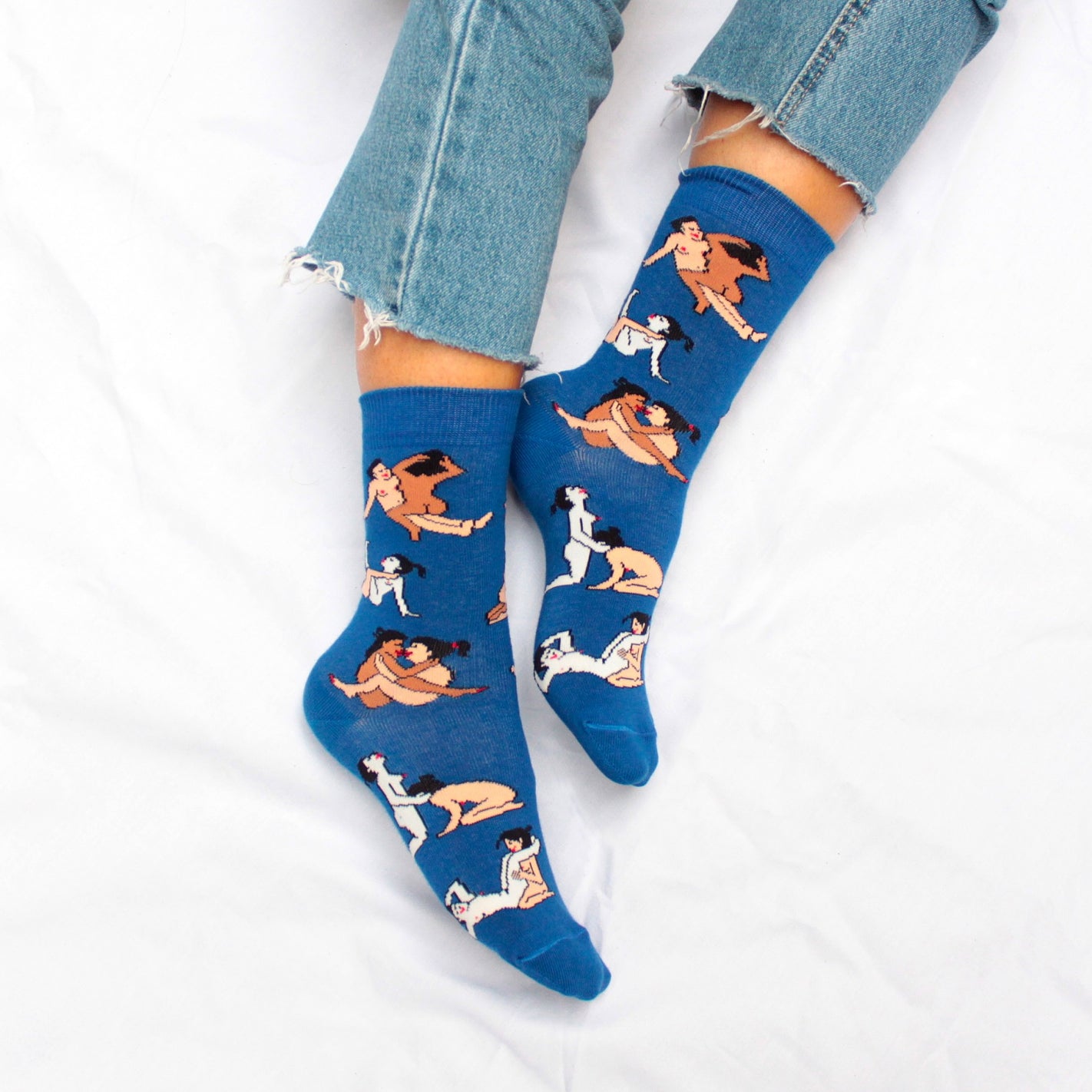 Shown on a light skinned models feet, a pair of women's CouCou Suzette cotton crew socks in deep blue with lesbian lovers engaging in varying Kama Sutra sex positions all over the socks.
