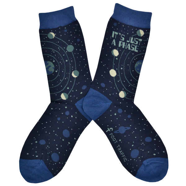 These blue cotton women's crew socks by the brand Foot Traffic feature small blue outlines of the planets  on the leg and foot and rings around the earth with the moon revolving in all its phases. The words "It's just a phase" are written at the top of the sock.