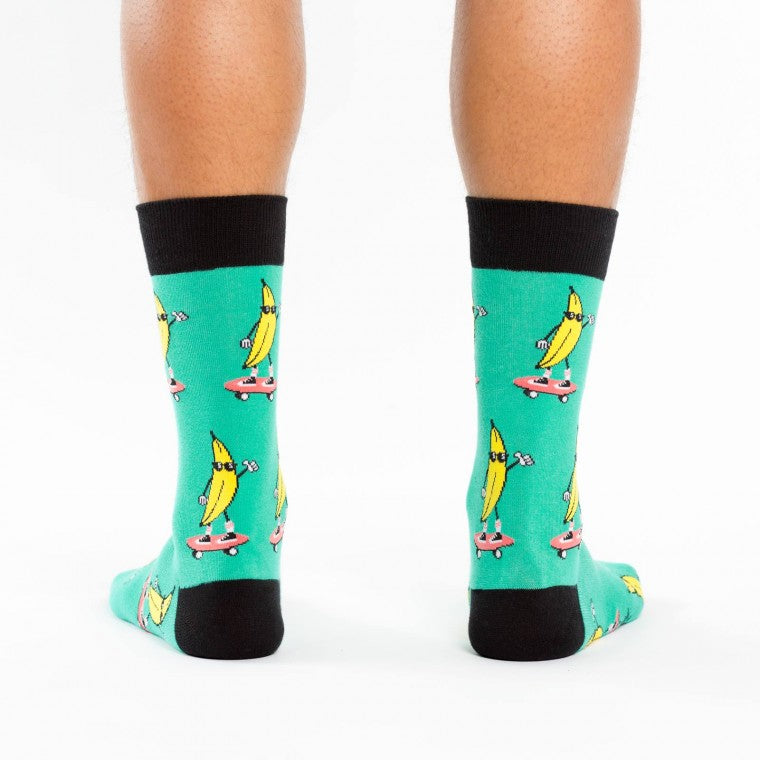 Shown on a model, a pair of Sock It To Me turquoise cotton men's crew socks with black cuff/heel/toe and goofy bananas skateboarding while wearing cool sunglasses