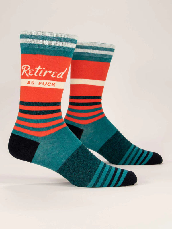 Pair of crew socks on foot forms, red with teal and black stripes, and a band of beige text that reads "RETIRED AS FUCK"