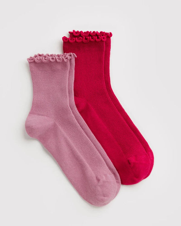 Two pairs of ribbed ankle socks with ruffled trim at the top, shown on a light gray background. One pair is a vivid red, and the other is a dusty rose pink.