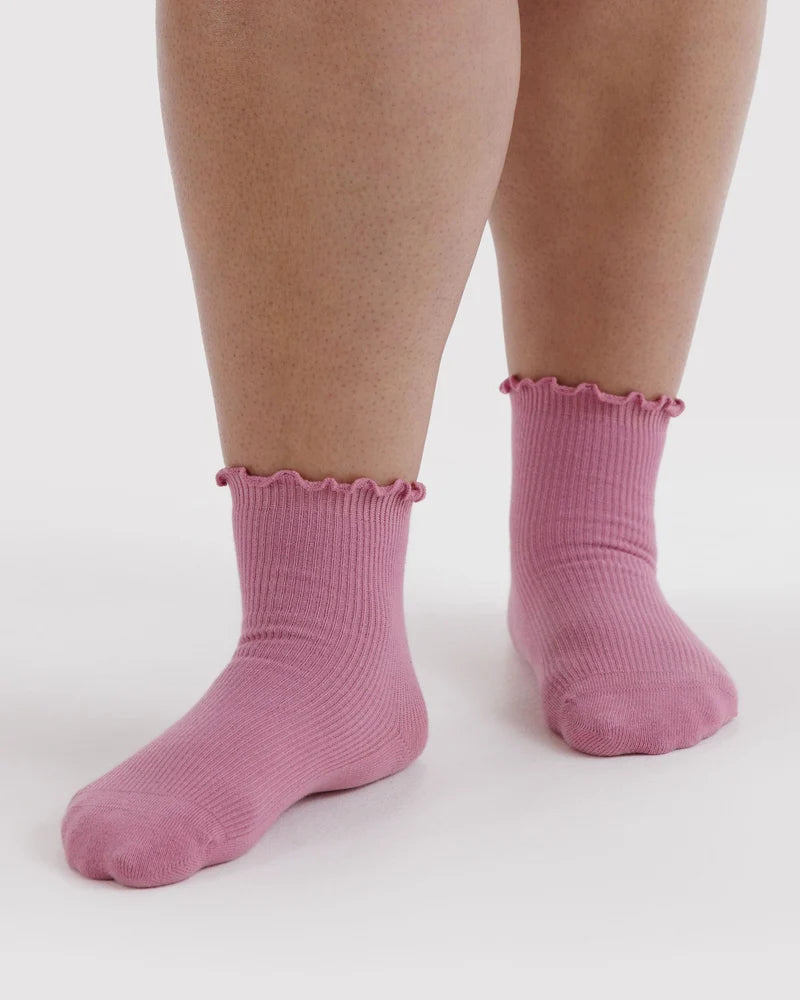 A pair of pink ribbed ankle socks with ruffled trim at the top, shown worn on a person's feet against a plain light background.