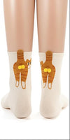 A model wears cream socks with orange cats and gold pompom balls