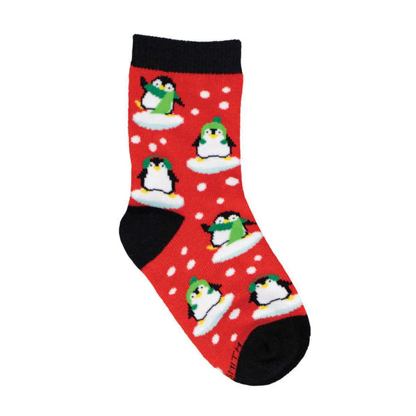 In flatlay, a red sock with black ankle, heel and toe featuring penguins in green hats, scarves and earmuffs in a snowy scene