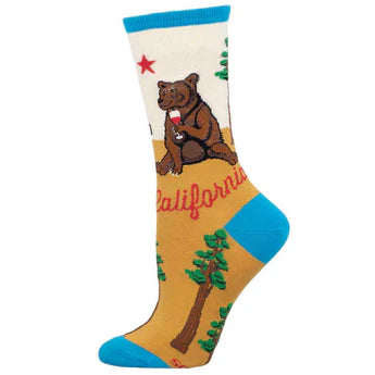 Foot form wears white and gold crew sock with blue heel, toe & ankle featuring redwood trees, a grizzly bear drinking a glass of red wine, a red star, red script that reads 