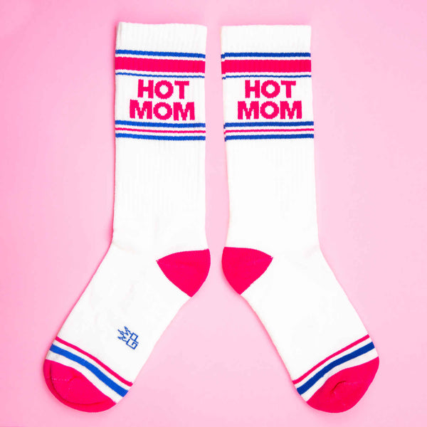 white athletic style socks with a hot pink toe and heel that say HOT MOM near the cuff along with some blue and pink stripes laying flat on a pink background