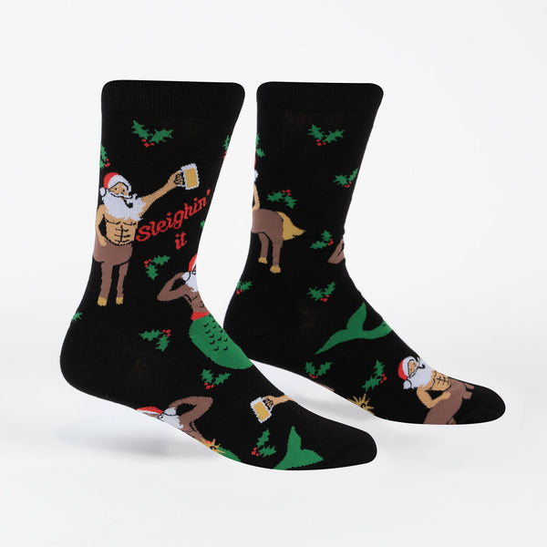 Two footforms wearing black crew socks with holly sprigs and Santa as a flexing merman and a centaur holding a beer stein. Red text reads "Sleighin' it".