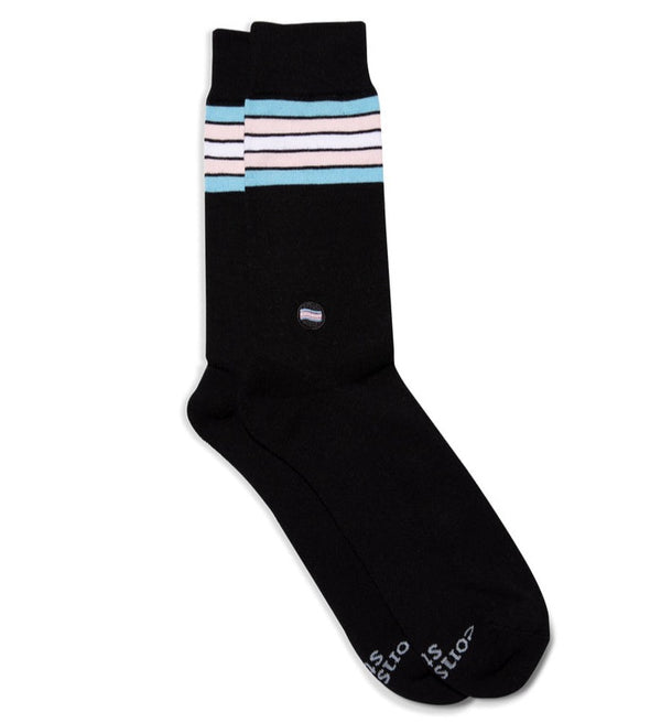 a pair of black socks laid flat with a small embroidered trans pride flag patch on the ankle and 5 stripes of blue, pink and white near the cuff symbolizing the trans pride colors