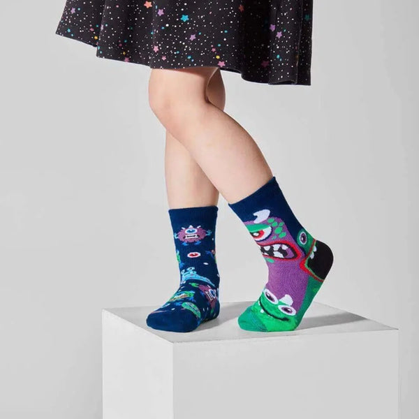 a small child photographed from the waist down wearing a black skirt with multicolored stars and a pair of mismatched navy blue socks with multicolored monsters and creatures all over them