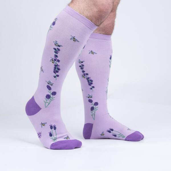 a pair of hairy legs wearing a pair of light purple knee high socks with a darker purple toe and heel covered in small purple flowers, green stems and small bees