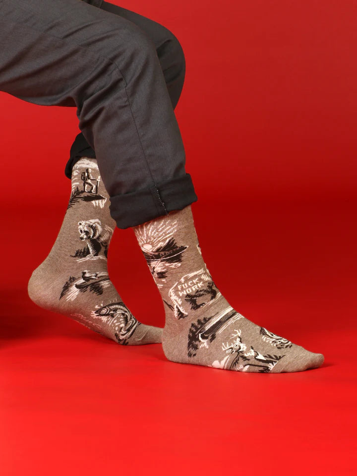 Model shown from legs down wearing light brown crew socks with designs of a fisherman at a mountain lake sunset, deer, canoes, and a bear with text that reads 