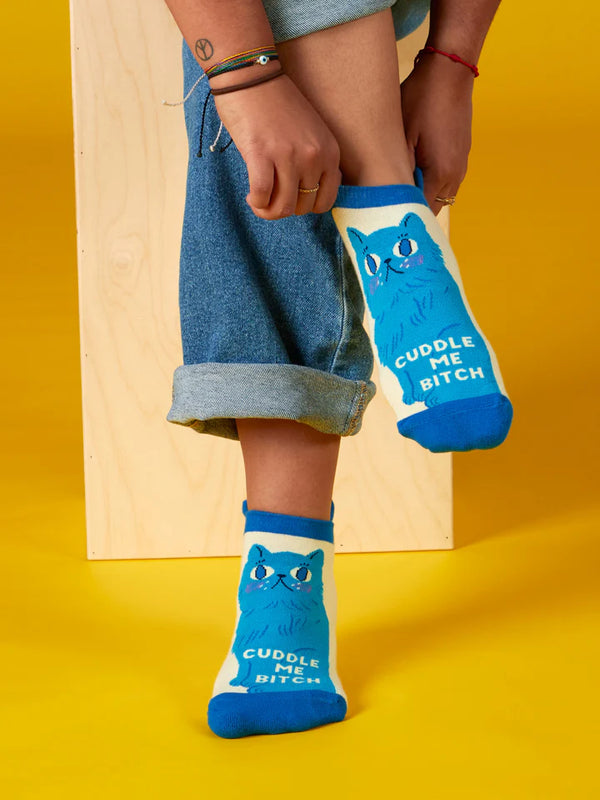 Person dons cream-colored ankle socks featuring a blue cat and text that reads "CUDDLE ME BITCH"