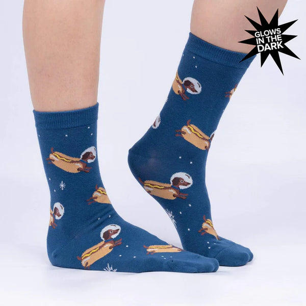 A model's feet wear blue crew socks featuring white stars and wiener dogs dressed as hot dogs wearing space helmets.