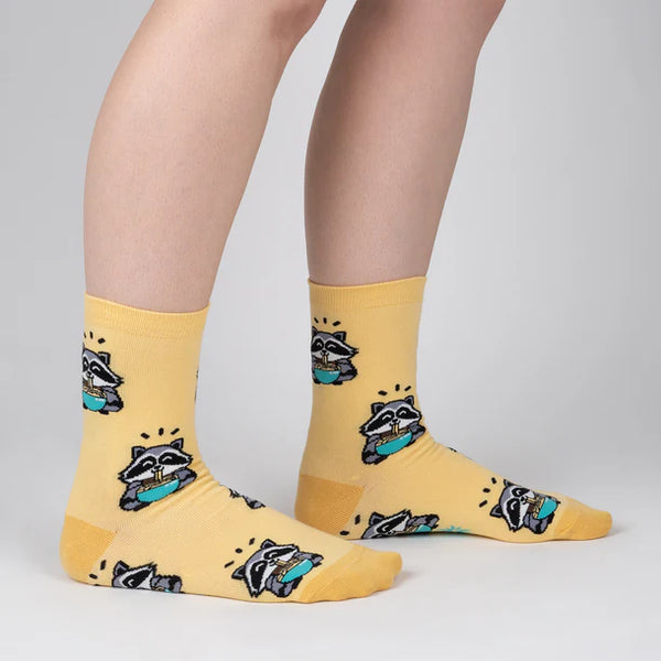 Model shown from knees down wears yellow socks featuring racoons eating ramen