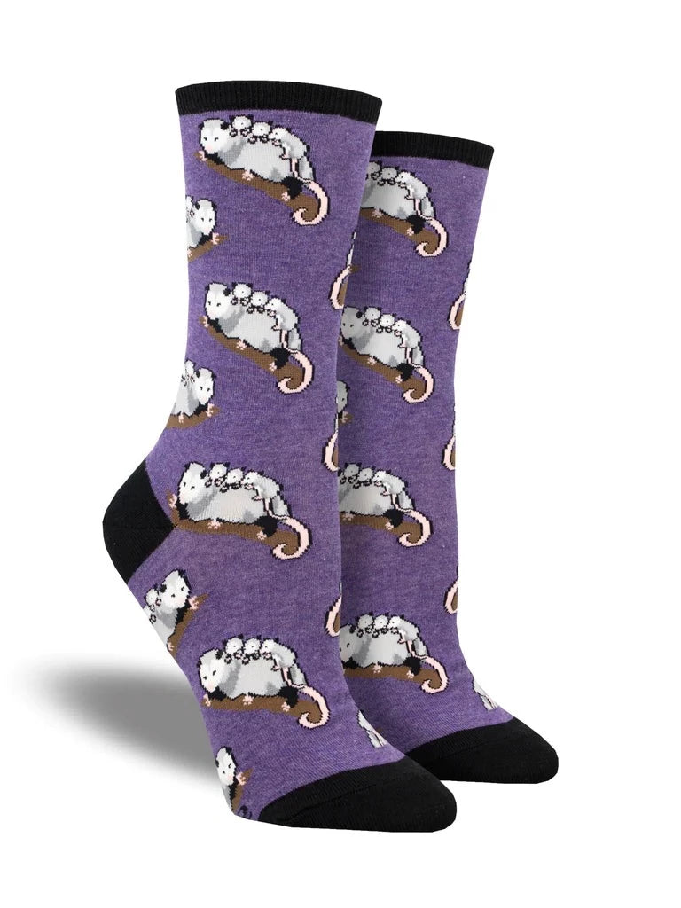 A pair of women's cotton crew socks in purple with a black heel, toe and, cuff that feature an all over motif of mother possums with their babies piled on their backs. 