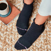 A model wears black ankle socks with lettuce edge tops on a carpet