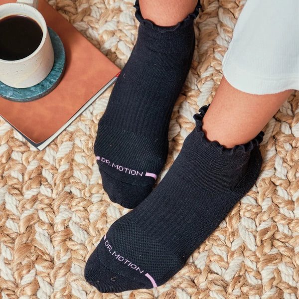 A model wears black ankle socks with lettuce edge tops on a carpet