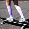 a cropped photo of a woman skateboarding while wearing sneakers and purple and white knee high socks
