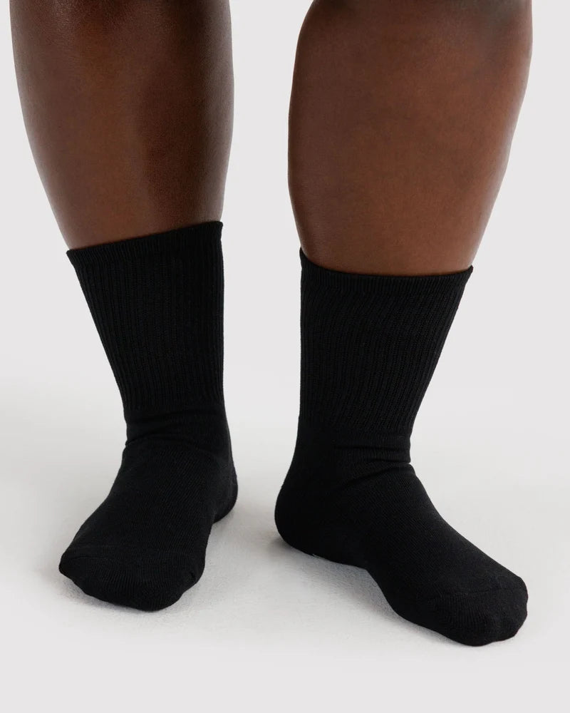 A close-up of a person's feet wearing plain black ribbed crew socks against a light gray studio background.