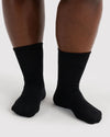 A close-up of a person's feet wearing plain black ribbed crew socks against a light gray studio background.