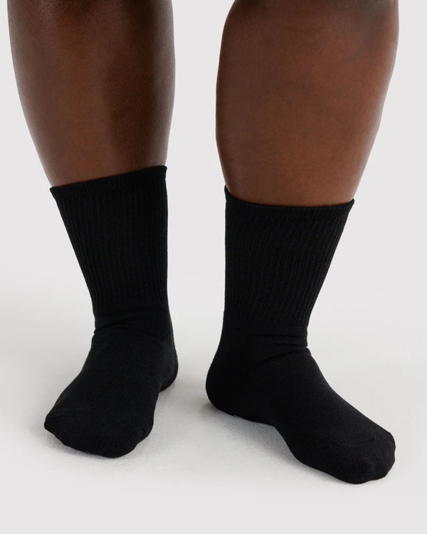 A close-up of a person's feet wearing plain black ribbed crew socks against a light gray studio background.