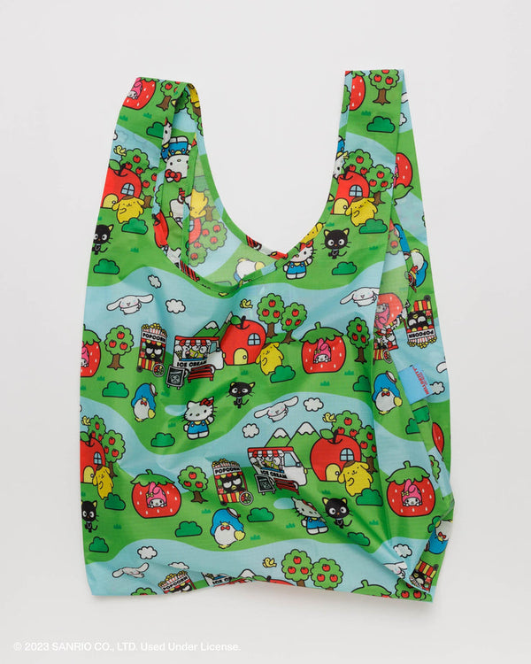 a reusable tote bag printed with a colorful illustration of Hello Kitty and her Sanrio friends, their fruit shaped homes and an Autumnal scene under a blue sky