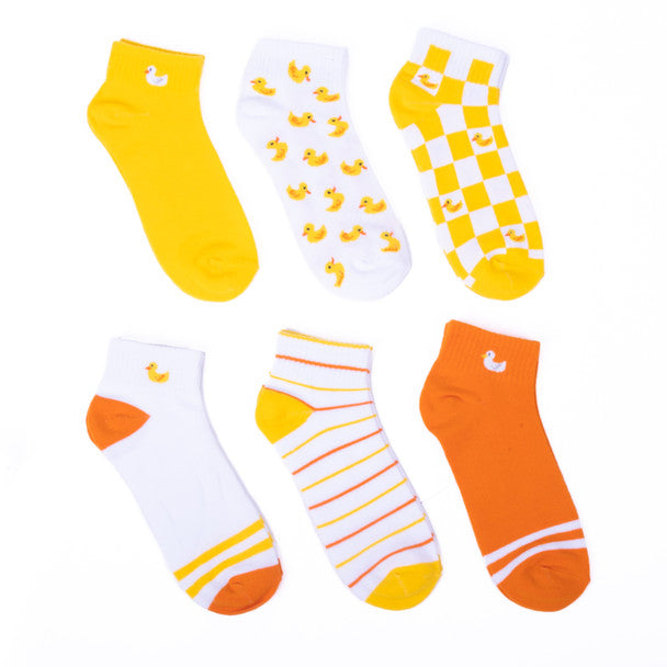 6 pairs of ankle socks are shown in flatlay on a white background: solid yellow with a white duck on the ankle, orange with white banding near the toe and a white duck on the ankle, white with yellow banding and a yellow duck, white with yellow ducks all over, white-and-yellow checks with yellow ducks in some of the white squares, and white with orange and yellow stripes