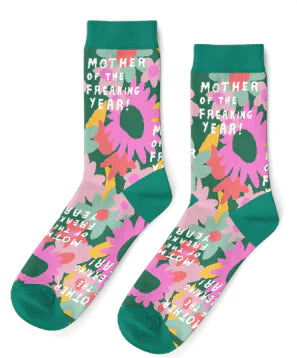 A pair of teal socks lie on a white background. They feature mint green, orange, pink, yellow and peach daisies drawn in spatter style and white text that reads 