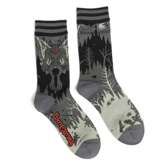 Shown in flatlay, 2 black socks with shadowy gray tree designs and a gray mothman with red eyes and fangs