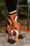 Model wears orange socks featuring black cats on skulls with moons and black lacy designs behind them