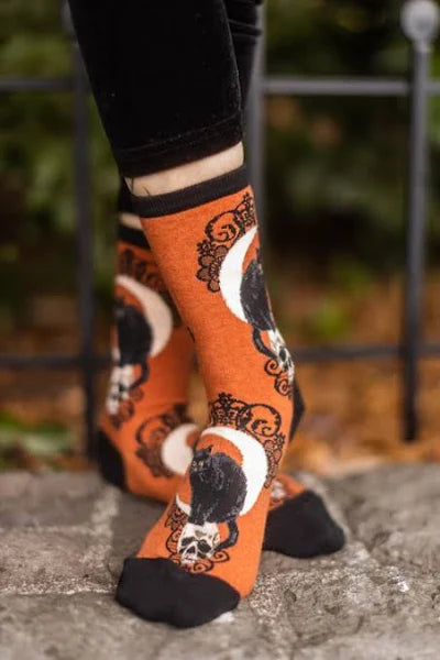 Model wears orange socks featuring black cats on skulls with moons and black lacy designs behind them