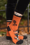 Model wears orange socks featuring black cats on skulls with moons and black lacy floral designs behind them