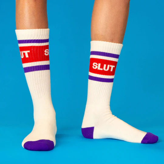 Model wears beige socks with red and purple stripes labeled 'SLUT'