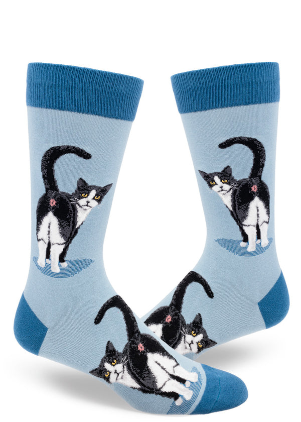 A pair of slate blue men's socks rests on a white background. The socks feature a prominent image of a tuxedo cat with its butthole in the viewer's face and its head turned to look at the viewer.