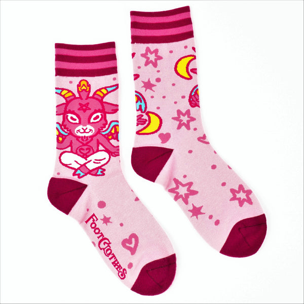 Shown in a flatlay, a pair of unisex crew socks in light pink with a dark pink heel and toe. The cuff is striped in magenta and hot pink. The leg depicts a hyper cute image of Baphomet with rainbow horns and wings. The rest of the socks has stars and hearts all over them.