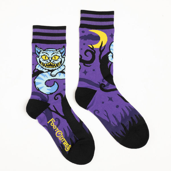 Shown in a flatlay, a pair of unisex crew socks in dark purple with a black heel and toe. The cuff is stripped purple and black while the leg of the sock features the Cheshire cat from Alice in Wonderland on a branch with the moon in yellow on the other side of the sock. The foot of the sock fades the tree down into black