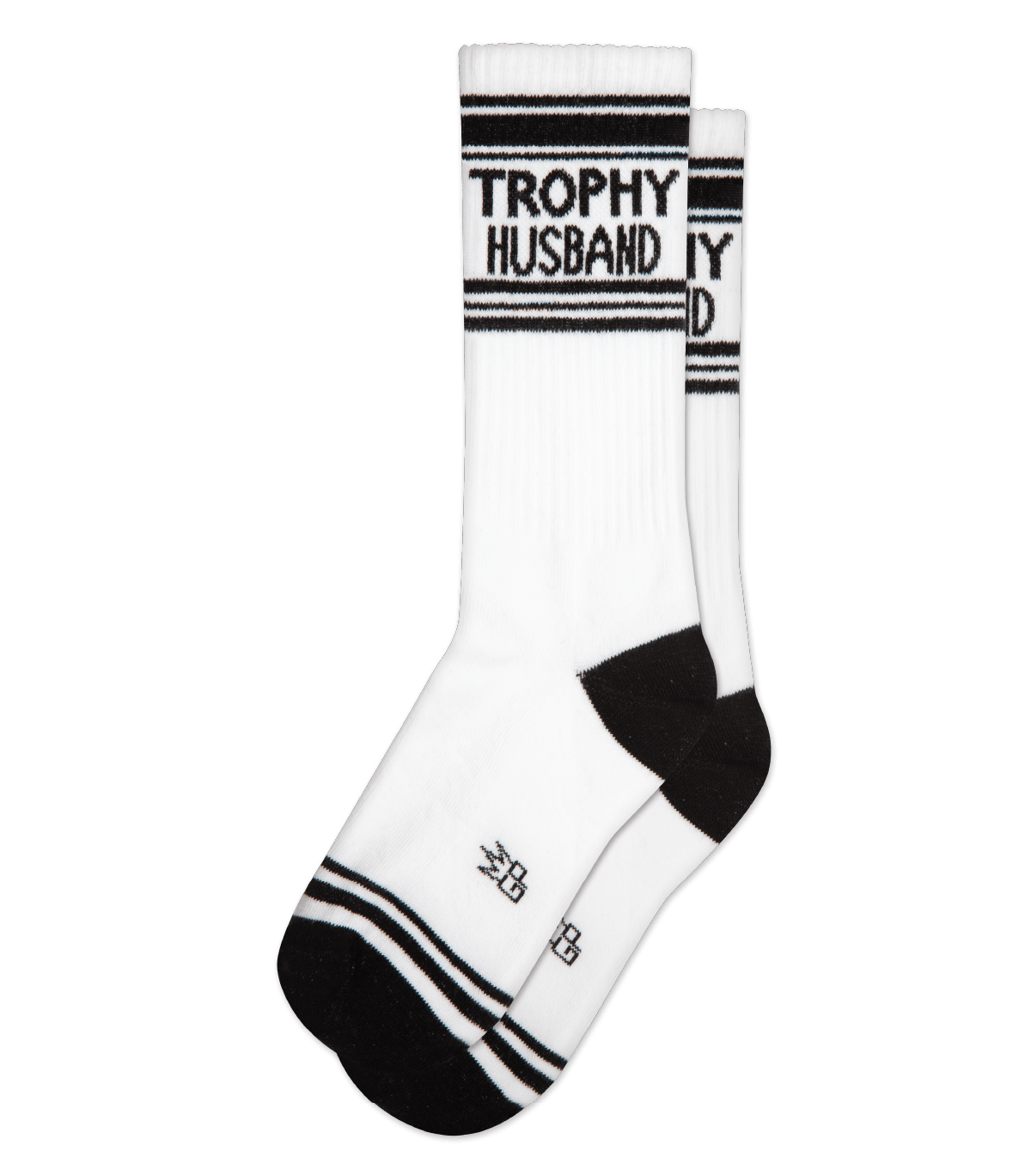 Shown in a flatlay, a pair of Gumball Poodle, white cotton crew socks with black heel/toe/accent stripes and “Trophy Husband” text