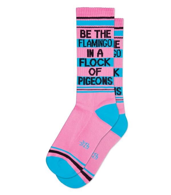 Shown stacked flat, a pair of unisex cotton crew Gumball Poodle brand sock in pink with black and teal stripes around the leg and a teal heel and toe. The text on the sock reads, "BE THE FLAMINO IN A FLOCK OF PIDGEONS".
