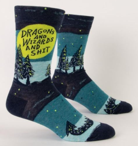 A pair of blue socks on foot forms featuring pine trees, a spiky dragons tail, and the text inside a lime green circle that says "dragons and wizards and shit"