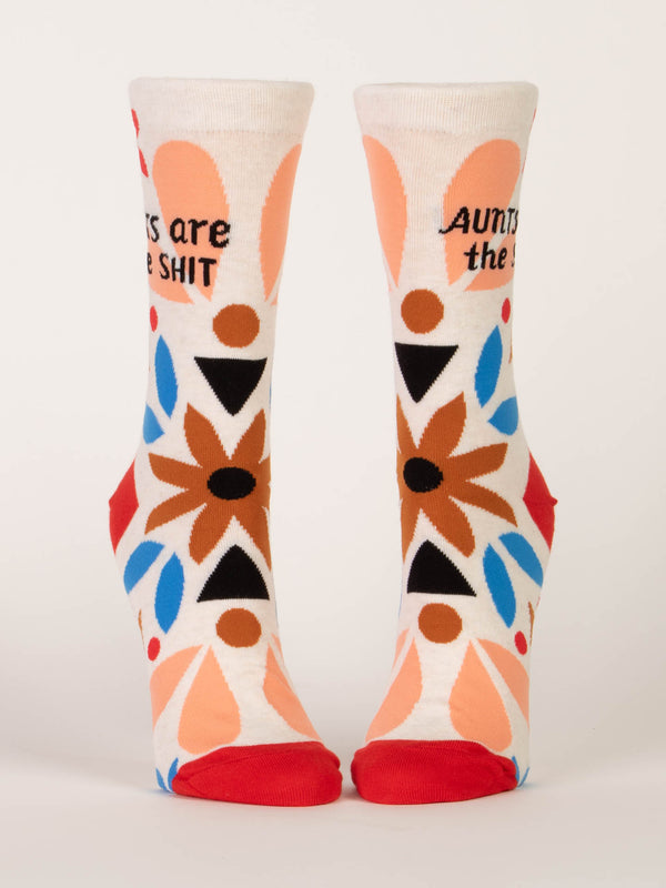 a pair of foot forms showing cream socks with a red toe and heel with black text that reads "aunts are the shit" and folk are inspired decorative shapes in blue, brown and black seen from the front