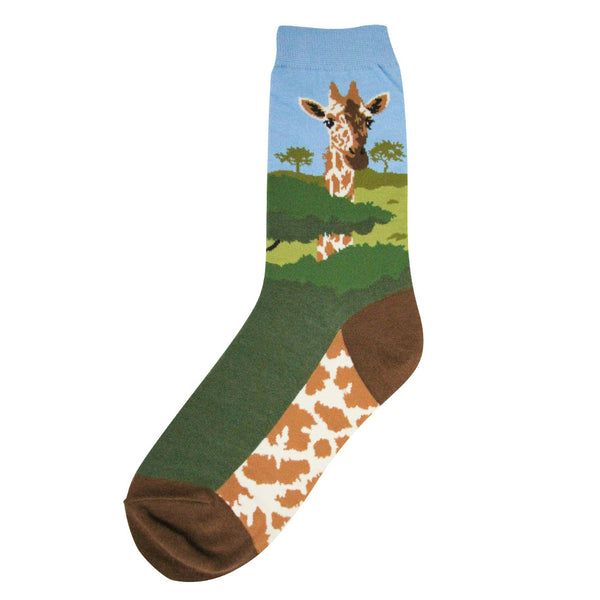 Shown in a flatlay, a single women's Foot Traffic brand cotton crew sock with a blue cuff and brown heel and toe. The leg of the sock has a giraffe head and neck with a savanna background. The foot is dark green on the top and the sole is a giraffe pattern.