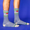 A person's feet and lower legs stand on a blue background. The feet wear gray socks that have tan heels, tan and green stripe patterns on the toe and ankle, and tan text that reads I [Red Heart Icon] Naps.