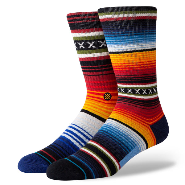 Shown in a flatlay, a pair of unisex Stance cotton crew socks with a subtly mismatched pattern of horizontal stripes in yellow, orange, blue, and white, inspired by Native American pattern