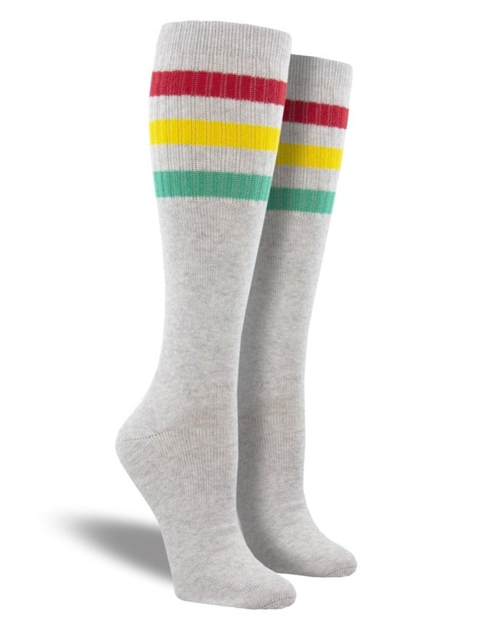 Shown on a leg form, these heathered light gray cotton unisex tall crew socks by the brand Socksmith have a green, yellow and red horizontal stripe hugging the calf.
