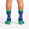 a childs legs seen from behind wearing a pair of blue socks with green heel and cuff and a pattern of dinosaur skeletons