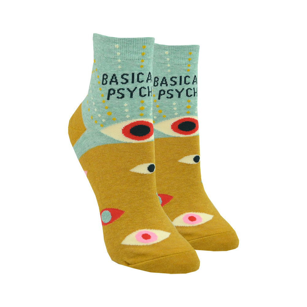 Shown on a leg form, a pair of Blue Q cotton women’s quarter length socks with mustard yellow and mint green background, mysterious eyes pattern, and “Basically Psychic” text