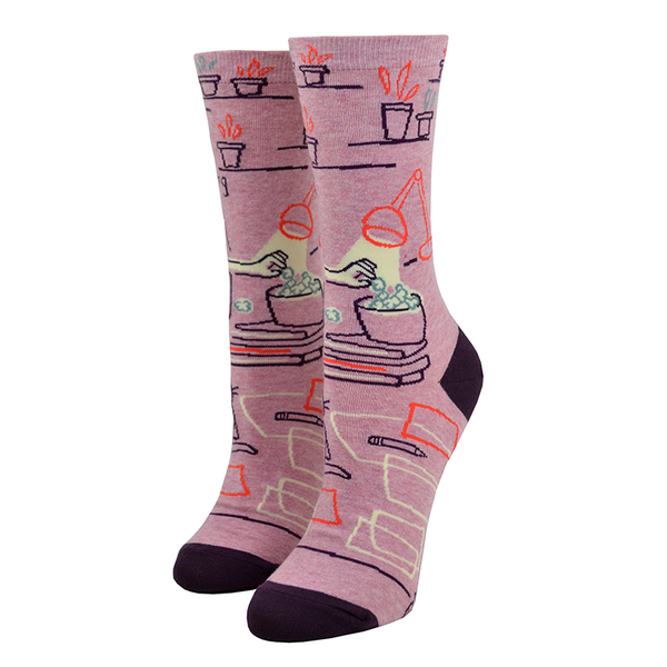 The reverse side of this "Go Away I'm Introverting" Blue Q women's cotton crew socks shows a hand reaching for popcorn and miscellaneous decorations like a desk lamp and plant!